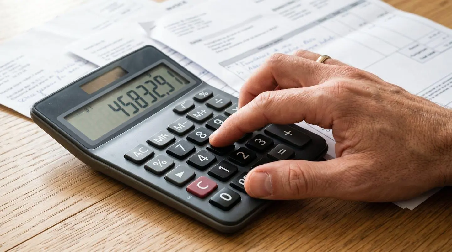 Gros plan sur une calculatrice moderne avec une main tapant des chiffres, des documents financiers floutés en arrière-plan sur un bureau clair